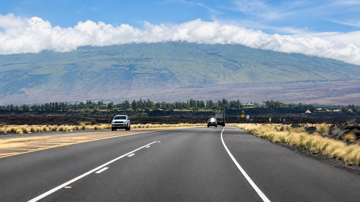 Clean open road through Hawaii lava fields toward a cloud-covered mountain