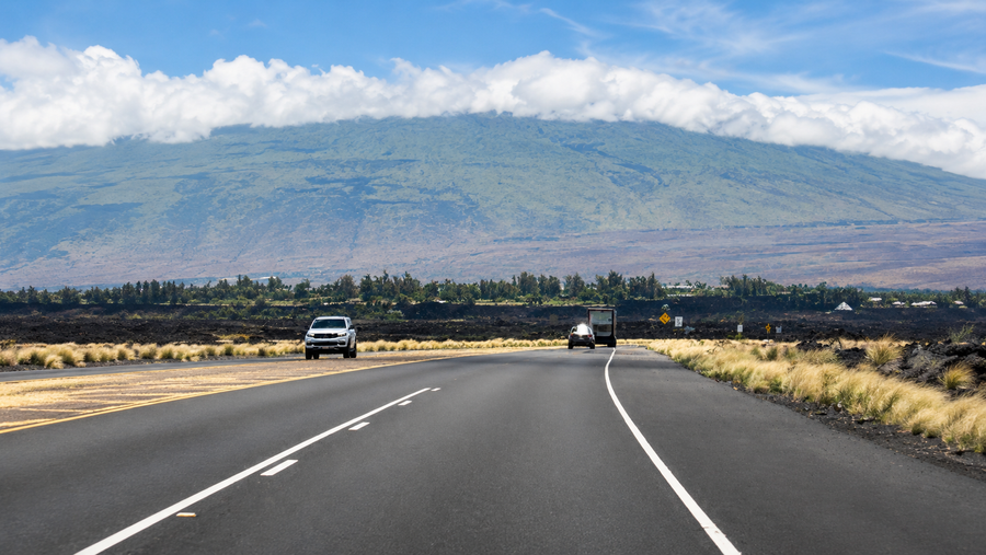 Clean open road through Hawaii lava fields toward a cloud-covered mountain